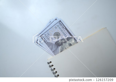 Top view of a pile of 100 dollar banknotes on a notebook with a white background. Copy space. Concept of wealth, saving or investment, and tax 126157209