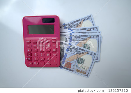Top view of pink calculator and a pile of 100 dollar banknotes on a white background. Concept of wealth, saving or investment, and tax 126157210
