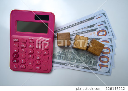 Top view of a pink calculator and a pile of 100 dollar banknotes with wooden cubes on a white background. Mockup or Copy space. Concept of wealth, saving or investment, and tax 126157212