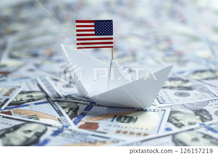 Paper boat with the USA or United States of America flag sailing on dollar banknotes. Concept of economy, financial or government Paper boat with the USA or United States of America flag sailing on dollar banknotes. Concept of economy, financial or government 126157219