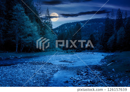mountain landscape with river at night. mysterious scenery with stones in the water and forest on the shore in full moon light. starry sky with dark clouds 126157639