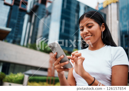 A young woman is engrossed in using her smartphone while situated in an urban environment A young woman is engrossed in using her smartphone while situated in an urban environment 126157854
