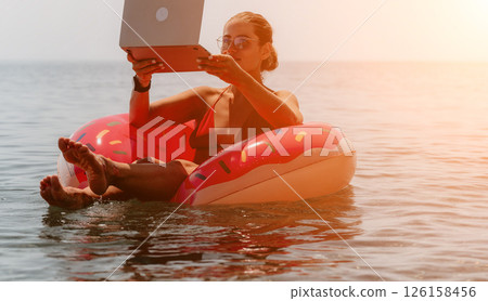 Laptop, Beach, Work - Woman Uses Laptop on Inflatable Float in Ocean Water Laptop, Beach, Work - Woman Uses Laptop on Inflatable Float in Ocean Water 126158456