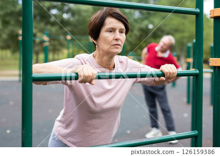 Elderly woman doing exercises on sports bars at outdoor sports ground 126159386