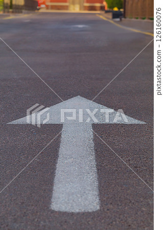 A symbol of moving forward in the form of a painted arrow on the asphalt in a narrow street of a residential area of the city. Symbolism of the path and achievement of the goal in life 126160076
