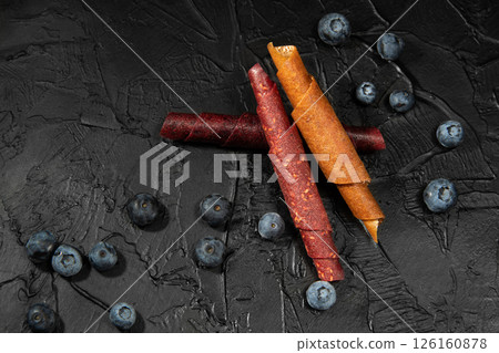 Fruit peel fruit in rolls. Pastille. Background for text and articles about healthy eating. Breakfast in hand. Raw food diet, vegan sweetness, dessert without sugar and flour. Bog whortleberry. Fruit peel fruit in rolls. Pastille. Background for text and articles about healthy eating. Breakfast in hand. Raw food diet, vegan sweetness, dessert without sugar and flour. Bog whortleberry. 126160878