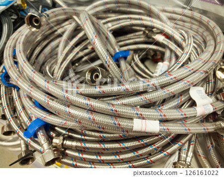 Flexible metal hoses coiled and ready for plumbing projects in a workshop Flexible metal hoses coiled and ready for plumbing projects in a workshop 126161022