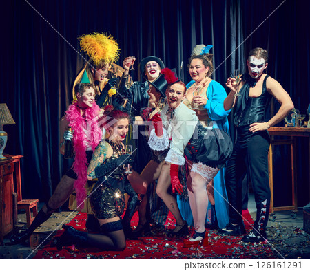 Cabaret group dressed in corsets top hats toasting dramatically with glasses over red carpet confetti. 126161291