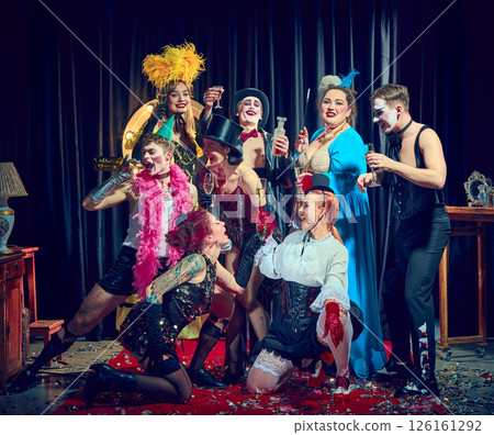 Joyful cabaret cast cheers holding champagne glasses with red gloves corsets feathers and confetti. Joyful cabaret cast cheers holding champagne glasses with red gloves corsets feathers and confetti. 126161292