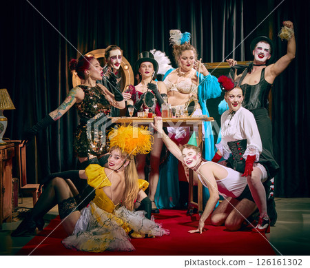 Cabaret performers in dramatic pose, wearing ornate costumes, feathers top hats, corsets, celebrating around table. Cabaret performers in dramatic pose, wearing ornate costumes, feathers top hats, corsets, celebrating around table. 126161302