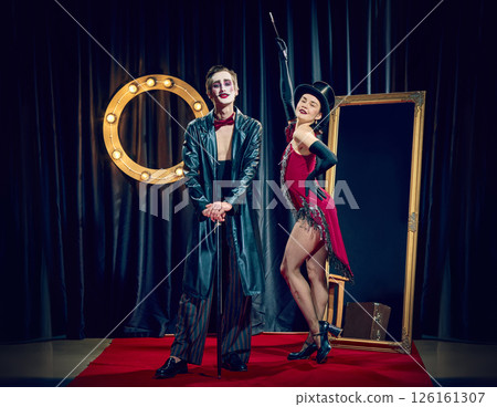 Stylized cabaret couple poses under lights wearing theatrical clothes cane hat and dramatic expressions. 126161307
