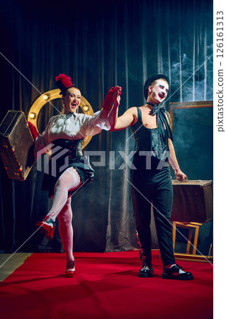 Joyful cabaret couple walks forward holding hands smiling in red gloves and hat with suitcases. Joyful cabaret couple walks forward holding hands smiling in red gloves and hat with suitcases. 126161313