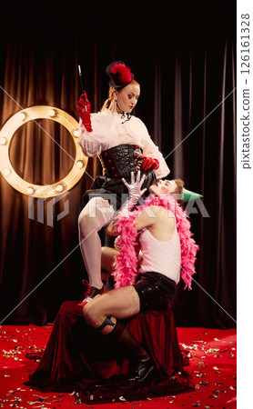 Two cabaret performers in striking vintage costumes, engage in dramatic pose on confetti-covered red carpet. Two cabaret performers in striking vintage costumes, engage in dramatic pose on confetti-covered red carpet. 126161328