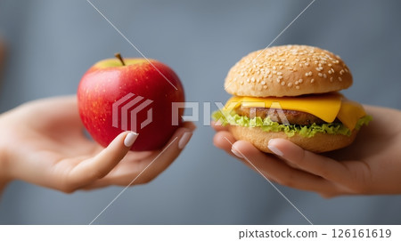 Comparing healthy eating choices with an apple in one hand and a cheeseburger in the other in a casual dining setting 126161619
