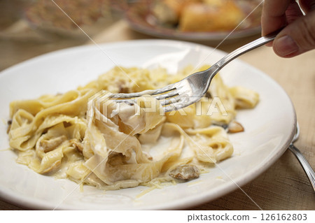 Creamy fettuccine pasta dish served on a white plate with fork lifting noodles for a delicious meal 126162803