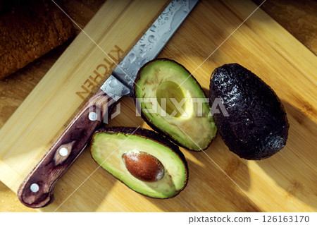 Three avocados and knife lie on the wooden cutting board. View from the top 126163170