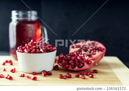 Ceramic bowl full od pomegranate seeds, cutted pomegranate and a glass of pomegranate juice on the background lie on the wooden cutting board 126163172