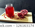 Glass of pomegranate juice and cutted pomegranate with seeds lie on a wooden cutting board on the concrete background 126163174