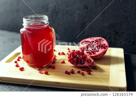 Glass of pomegranate juice and cutted pomegranate with seeds lie on a wooden cutting board on the concrete background 126163174