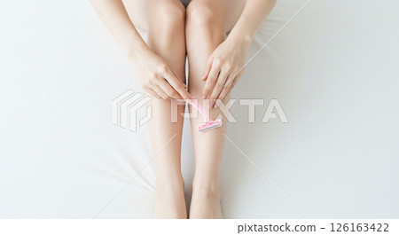A woman removing unwanted hair from her legs with a razor 126163422