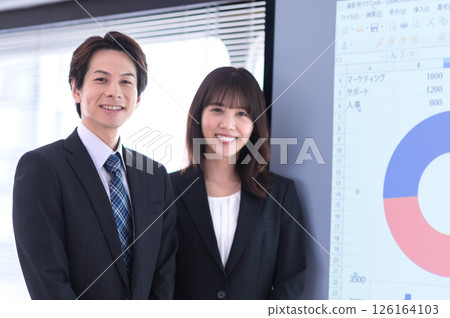 A man and a woman in suits standing in front of a screen in a conference room 126164103