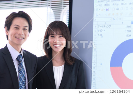 A man and a woman in suits standing in front of a screen in a conference room A man and a woman in suits standing in front of a screen in a conference room 126164104