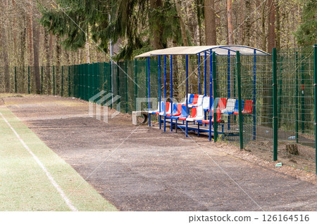 Empty bench and covered dugout overlooking playing field surrounded by forest Empty bench and covered dugout overlooking playing field surrounded by forest 126164516