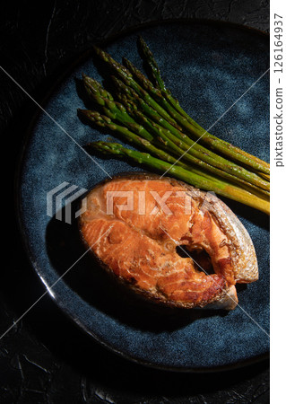 Fried salmon fillet with green asparagus on a dark background. Fried salmon fillet with green asparagus on a dark background. 126164937