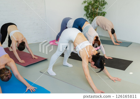 Yoga class Pilates workout. Group of sporty people doing exercise in studio class for yoga wellness mindfulness meditation. Personal trainer men women practicing yoga in gym training stretching indoor Yoga class Pilates workout. Group of sporty people doing exercise in studio class for yoga wellness mindfulness meditation. Personal trainer men women practicing yoga in gym training stretching indoor 126165811
