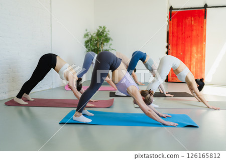 Yoga class Pilates workout. Group of sporty people doing exercise in studio class for yoga wellness mindfulness meditation. Personal trainer men women practicing yoga in gym training stretching indoor 126165812