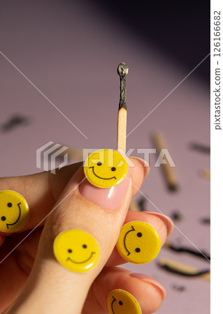 A burnt match in a hand among many matches on a light purple background. Yellow emoticons, creative. 126166682