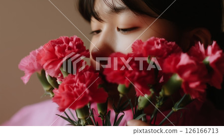 Young woman enjoys vibrant red carnations while posing with a thoughtful expression in a soft-lit room Young woman enjoys vibrant red carnations while posing with a thoughtful expression in a soft-lit room 126166713
