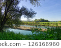 River landscape showing green vegetation, trees, and blue sky with contrails 126166960