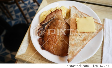 close up of Hong Kong style high calories breakfast of a pork chop, butter block on toast bread and pan fried sunny side up egg on a white plate 126167264