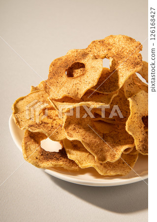 Dehydrated apple slices with powdered cinnamon on a plate. Close-up studio photo. 126168427