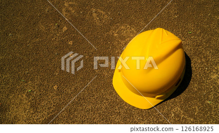 A Yellow safety helmet on bare soil, representation early - stage development, rural construction or disaster recovery effort, infrastructur growth. 126168925