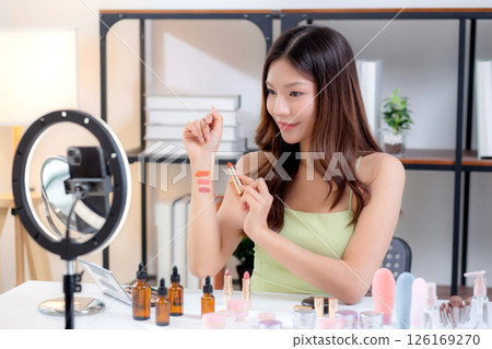 Young asian beauty influencer testing multiple lipstick shades on arm while recording makeup review. 126169270