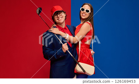 Happy couple hugging, smiling with golf club in hand, wearing colorful stylish outfits on red blue background. Happy couple hugging, smiling with golf club in hand, wearing colorful stylish outfits on red blue background. 126169453