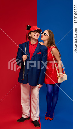 Woman blowing kiss to man smiling holding golf club on red blue split background wearing colorful outfits. Woman blowing kiss to man smiling holding golf club on red blue split background wearing colorful outfits. 126169503