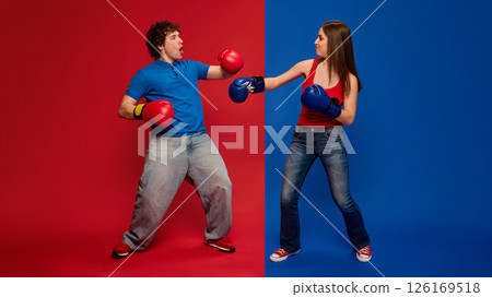 Energetic young man and woman, couple wearing boxing gloves and playfully engaged in mock fight Energetic young man and woman, couple wearing boxing gloves and playfully engaged in mock fight 126169518