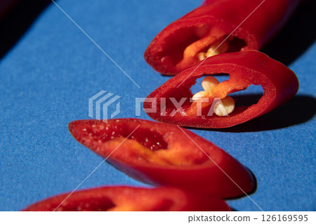 Red chili pepper in a cut closeup with pits on a blue background. Shadows. Macro. Red chili pepper in a cut closeup with pits on a blue background. Shadows. Macro. 126169595