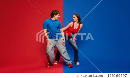 Young man and woman, couple in dynamic poses, dancing, wearing blue and red tops with jeans, smiling at each other Young man and woman, couple in dynamic poses, dancing, wearing blue and red tops with jeans, smiling at each other 126169597