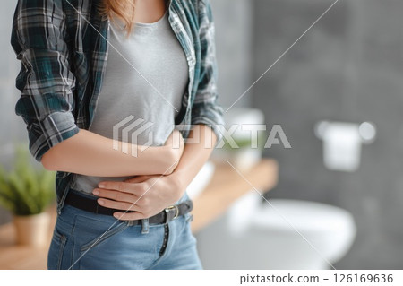 A young woman holding her stomach with her hands in the toilet. Image of poor health representing stomachache, stomach pain, and stress 126169636