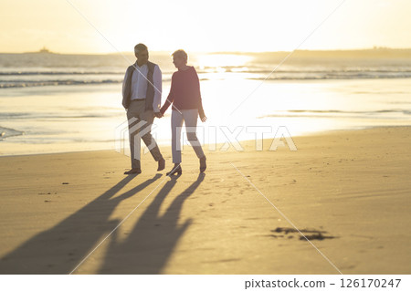 Senior couple walking on beach at sunset holding hands Senior couple walking on beach at sunset holding hands 126170247
