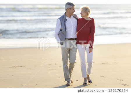 Happy senior couple walking on the beach at sunset 126170254