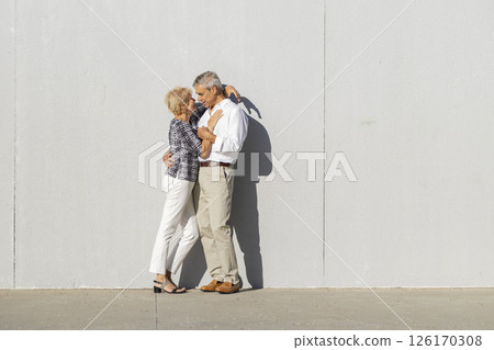 Senior couple embracing tenderly against a gray wall Senior couple embracing tenderly against a gray wall 126170308