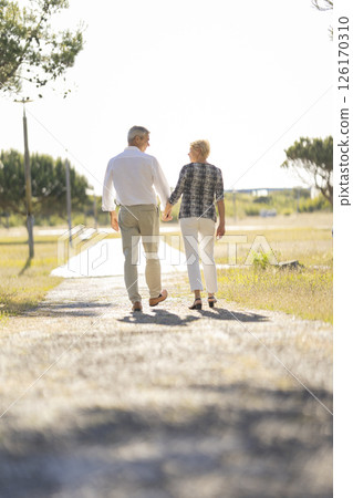Happy senior couple walking on a path holding hands Happy senior couple walking on a path holding hands 126170310