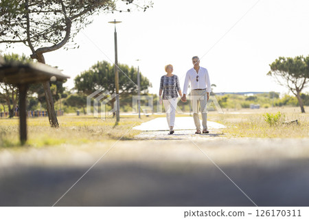 Senior couple walking in park holding hands on sunny day Senior couple walking in park holding hands on sunny day 126170311