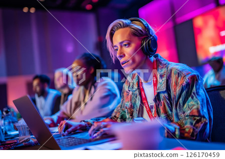 Woman working on laptop at lively conference surrounded by creative professionals 126170459
