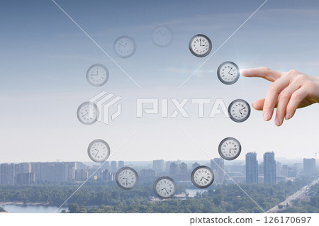 Hand points towards floating clocks in a city skyline. Hand points towards floating clocks in a city skyline. 126170697
